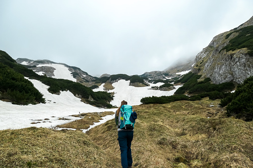 Woman with backpack on a hiking trail with view on cloud covered mountain peaks of the Hochschwab Region in Upper Styria, Austria. Plateau full of snow in beautiful Alps, Europe. Freedom vibe. Rain