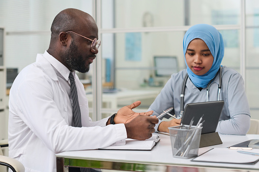 African American doctor pointing at tablet pc and discussing difficult disease with his colleague during a meeting in office