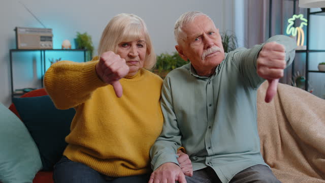 Upset senior family showing thumbs down, dislike bad work, disapproval dissatisfied feedback at home