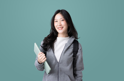 Young Asian girl college student with tablet and backpack isolated over teal background