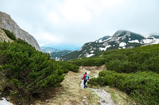 Woman with backpack on a hiking trail with view on cloud covered mountain peaks of the Hochschwab Region in Upper Styria, Austria. Plateau full of bushes in beautiful Alps, Europe. Freedom vibe. Rain