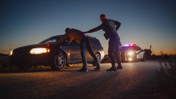 A Professional Middle Aged Policeman Performing a Pat-Down Search on a Fellon With his Hands on Car Hood. Documentary-like Shot of Procedure of Arresting Suspects. Experienced Cop Looking for Weapons A Professional Middle Aged Policeman Performing a Pat-Down Search on a Fellon With his Hands on Car Hood. Documentary-like Shot of Procedure of Arresting Suspects. Experienced Cop Looking for Weapons driving under the influence stock pictures, royalty-free photos & images
