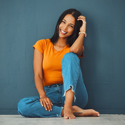 Black woman, floor and home with smile by wall for clothes, relax and fashion with barefoot. Gen z girl, model portrait and happy in house with feet, jeans and happiness on face by blue background