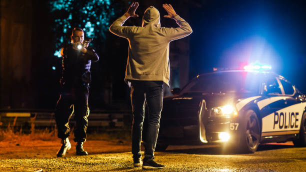 policial caucasiano de meia-idade mira em um suspeito. polícia usando uma arma para intimidar criminoso procurado. suspeito levantando as mãos em conformidade. polícia faz prisão com sucesso - threats men african descent caucasian - fotografias e filmes do acervo