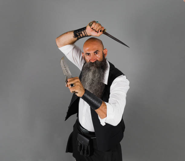istock a head shaved man with long beard holding two knives while looking at camera ahead a gray background 1480290725