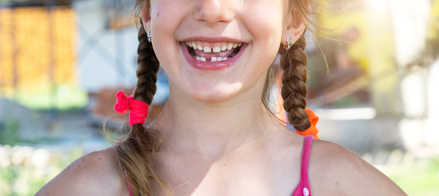 Toothless happy smile of a girl with a fallen lower milk tooth close-up. Changing teeth to molars in childhood