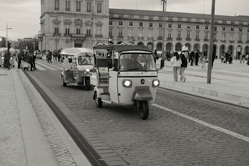 Lisbon, Portugal - November 19, 2022: A tuk-tuk rides along a street in the Praça do Comércio square Lisbon downtown.