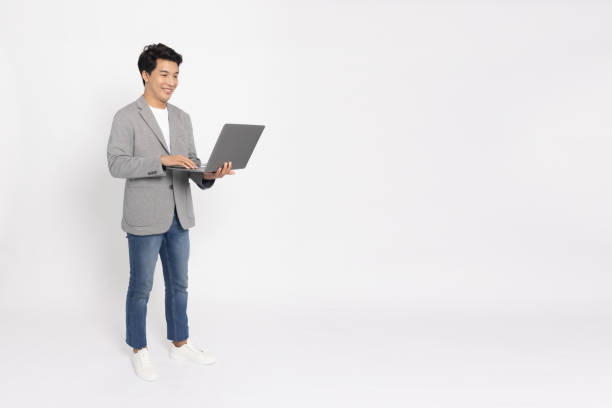 istock Happy young Asian business man using laptop computer and standing isolated on white background, Full body composition 1480291796