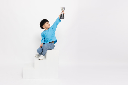 Happy Asian little boy holding trophy and sitting on stairs isolated on white background, Full length and five years old