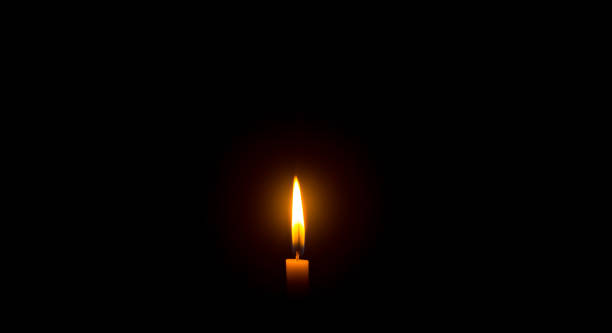 istock A single burning candle flame or light glowing on an orange candle on black or dark background on table in church for Christmas, funeral or memorial service with copy space 1480294394