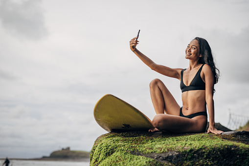 One woman, beautiful female surfer taking a selfie with smart phone by the sea.