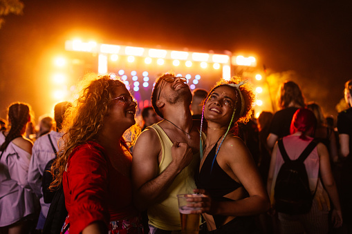 Three young Caucasian and beautiful friends drinking beer and having fun on a music festival