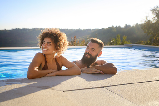 Young couple having fun at a swimming pool. Both about 25 years old, multiracial people.