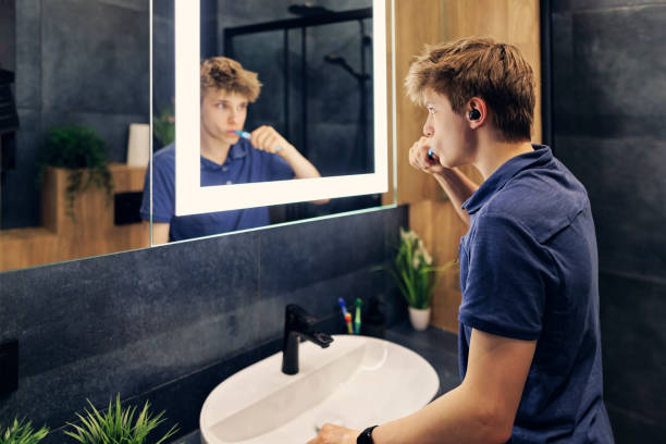 un adolescent se prépare à sortir dans une salle de bain sombre et moderne - side view mirror audio photos et images de collection