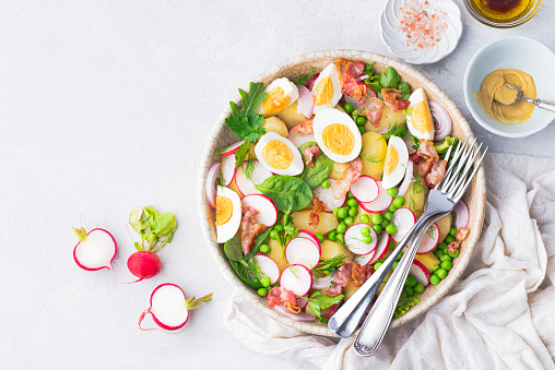 Summer fast balanced salad with baby potatoes, fried bacon, radishes, farmer organic  eggs and green peas and herbs, seasoned with olive oil, mustard sauce, balsamic and lemon.  Spring balanced diet, clean healthy lunch