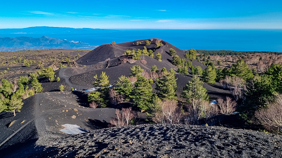Scenic view on crater of Sartorio on volcanic landscape of volcano mount Etna, in Sicily, Italy, Europe. Solidified lava, ash, pumice fields of erupted crater. Bare terrain with view in Ionian sea