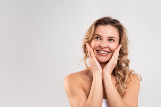istock Beautiful middle aged lady wrapped in towel touching cheeks and looking away 1480307724