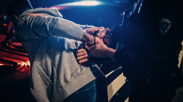 un policier force un civil docile sur le capot d’une voiture de police. l’agent a violemment poussé l’homme contre la voiture et l’a menotté. cas choquant de brutalité policière. gros plan sur les mains - civil rights photos et images de collection