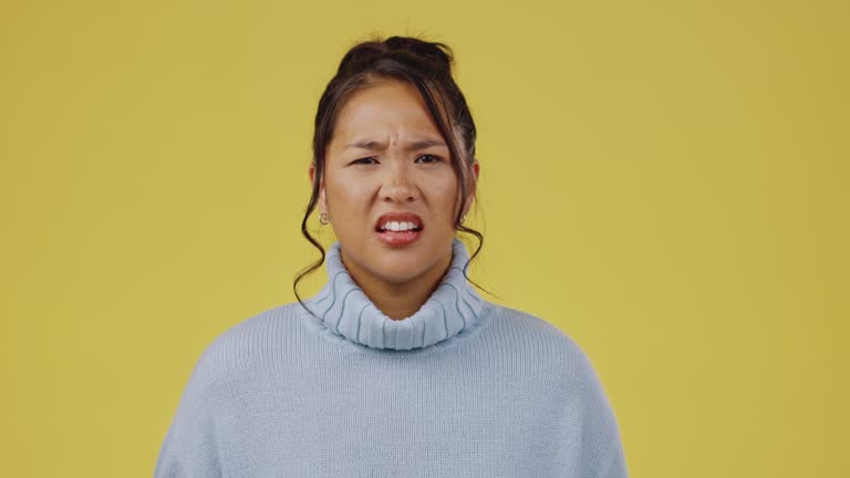 Asian woman, excited and disappointed face portrait in studio on a yellow background isolated space. Female model person confused with emoji and a frown for bad news or announcement on color