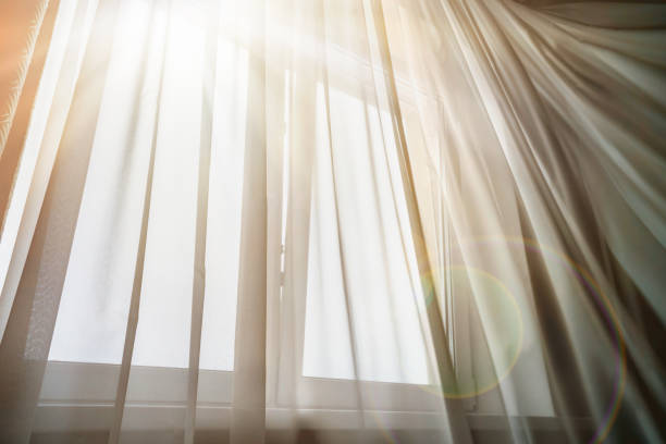 Bright sunrays lighting in house room through thin white curtain