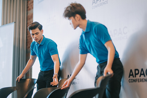 2 Asian crew arranging VIP speaker seat on stage before the business conference seminar begin