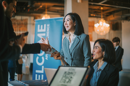 Asian businesswoman greeting all guest registering at reception desk attending business conference seminar