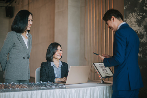 Asian businesswoman greeting all guest registering at reception desk attending business conference seminar