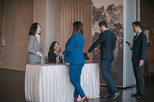 Asian businesswoman greeting all guest registering at reception desk attending business conference seminar
