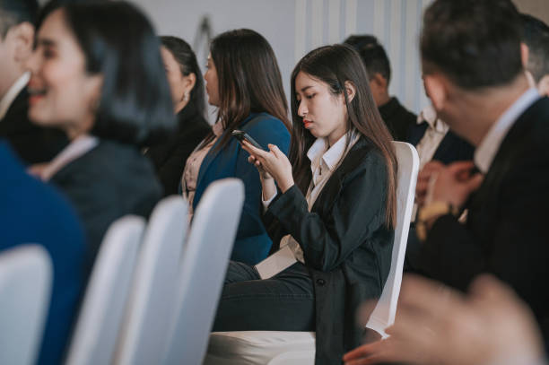 istock Asian Chinese seminar female participant using smart phone text messaging while waiting in business conference room 1480316887