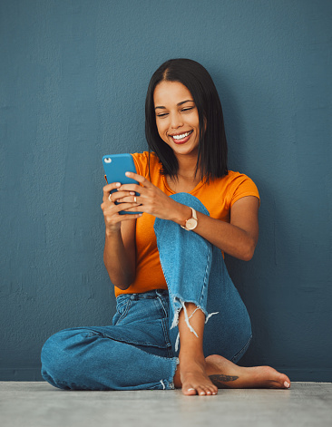Happiness, black woman on floor and smartphone for connection, smile and communication on dark studio background. Female, lady and cellphone for typing, texting and social media for online reading