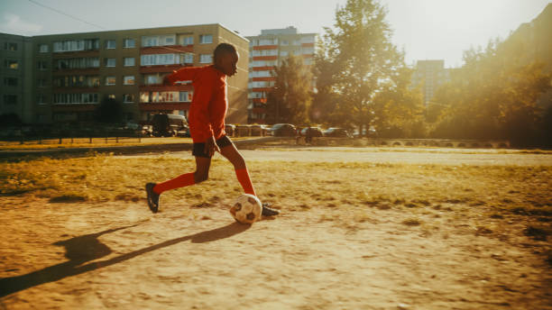 istock Young Talented Black Boy Practising Dribbling with Soccer Ball and Shooting Free Kicks. Talented Football Player Practicing Scoring Goals in the Backyard. 1480320229
