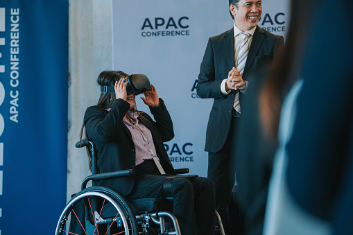 Asian Indian woman in wheelchair trying VR goggle during business conference seminar in convention center