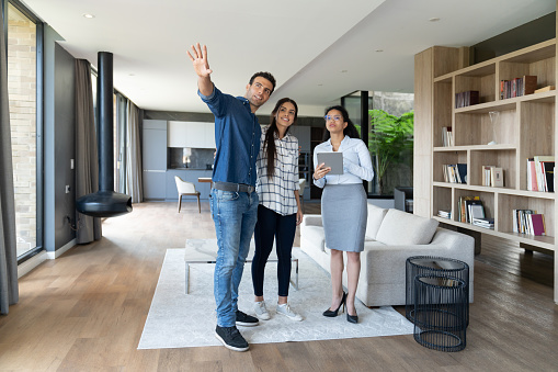 Real estate agent showing a house to a young Latin American couple and man pointing away - home ownership concepts