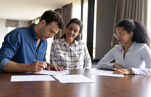 Happy Latin American couple buying a house and signing the deed in front of their real estate agent - home ownership concepts