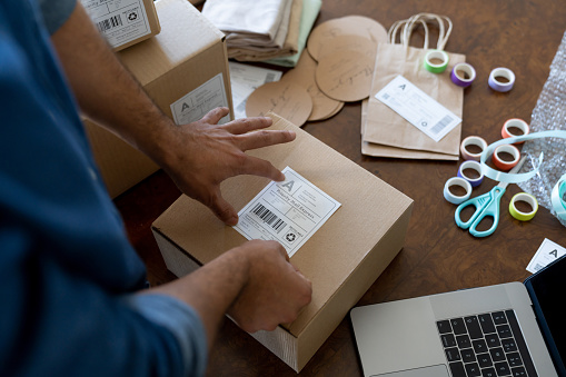 Close-up on a businessman working at home and pasting a label while shipping orders