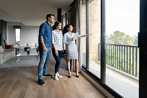 Real estate agent showing a house for sale to a couple and looking at the view -home ownership concepts