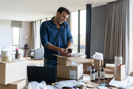 Busy Latin American businessman multi-tasking while packing some orders for his e-commerce business - entrepreneurship concepts