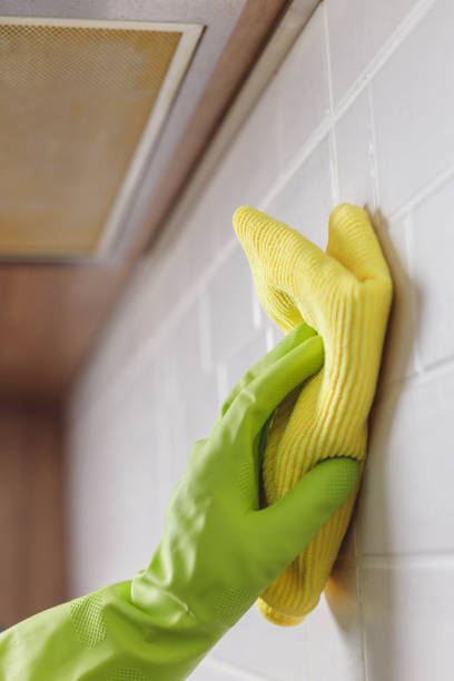 istock Hand in Gloves Washing White Tiled Wall in Kitchen with Yellow Microfiber and Spray Bottle with Detergent 1480324966