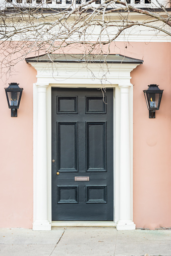 A colonial era door with gas lanterns and a mail slot on a pink house.