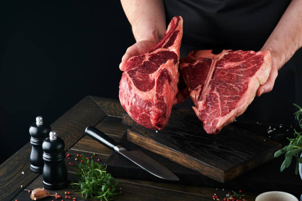 istock Chef cutting steak beef. Mans hands hold raw steak Tomahawk on rustic wooden cutting board on black background. Cooking, recipes and eating concept. Selective focus. 1480329613