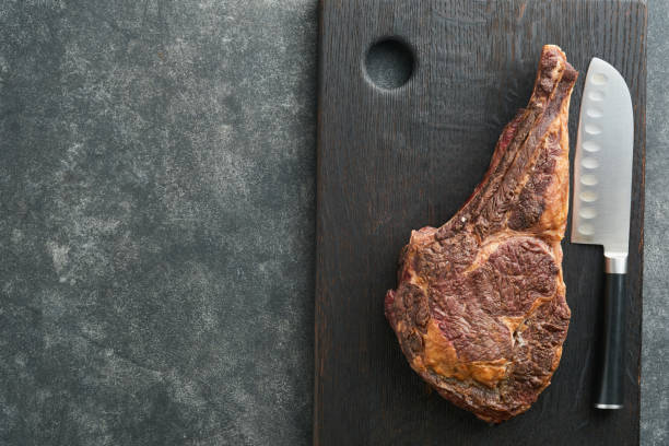 istock Tomahawk steak. Sliced grilled tomahawk beef steak with baked cherry tomatoes, herbs and salt on old wooden background. Preparing to grill.  Top view and copy space. 1480329672