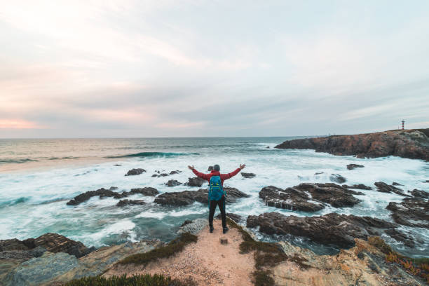 istock Fearless man with a backpack watching the sunset over the Atlantic Ocean in Porto Covo, Portugal. A hiker stands on the edge of a cliff looking into his future. Self-awareness 1480331114