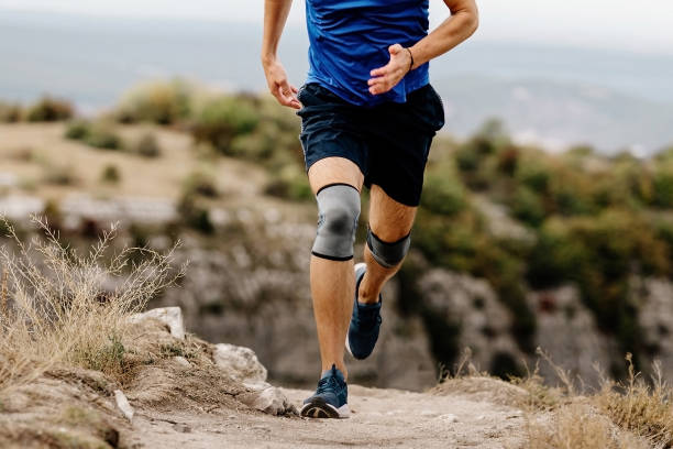 male runner with knee pads running on mountain trail, protective compression sleeves against injuries to stabilize legs male runner with knee pads running on mountain trail, protective compression sleeves against injuries to stabilize legs kneepad stock pictures, royalty-free photos & images