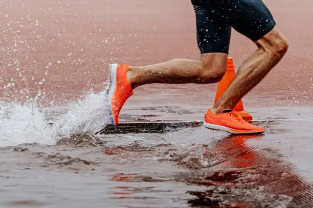 legs male athlete runner running steeplechase race, championship athletics competition, water splashes