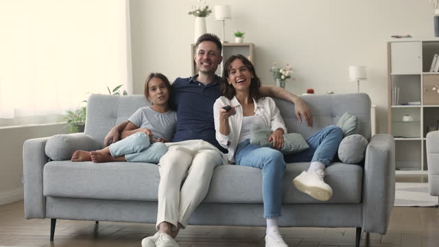 Family with daughter watching TV seated on sofa at home