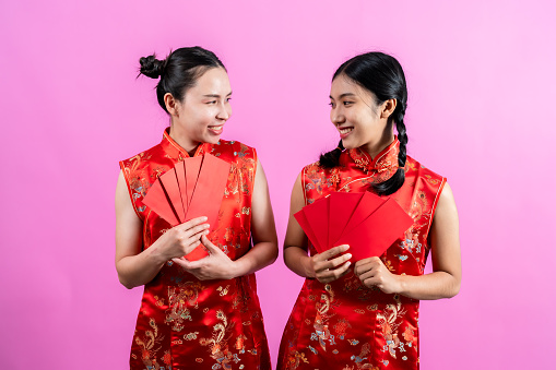 portrait, Two Asian girls wearing red Chinese national costumes (cheongsams), Both of them were holding red envelopes, or as Chinese people call angbao, Isolated indoor studio on blue background.