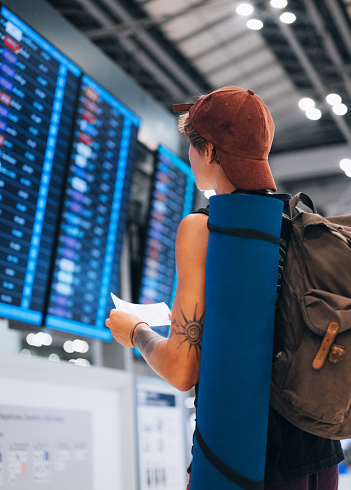 A young man checking his flight on the departure board. He holds  a plane tickets in his hands. Travel concept