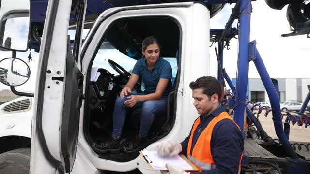 Male worker at a car distribution center asking female car transporter to sign before leaving with a load of new cars
