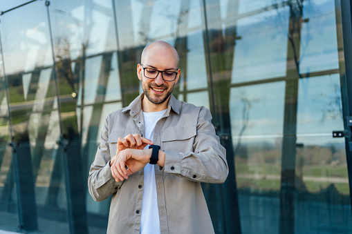 Young smiling man checking notification on his smartwatch outdoors