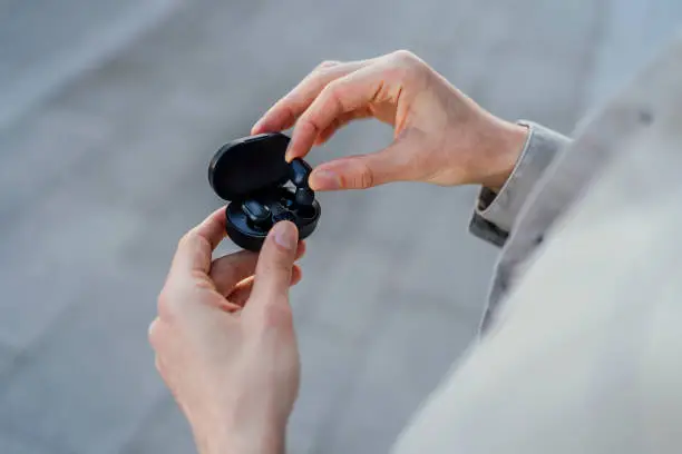 Man taking out a black wireless earbud from charging box outdoors